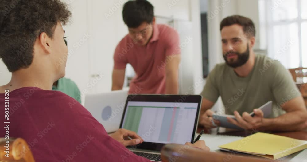 Happy diverse male friends talking and using laptop in living room Happy diverse male friends talking and using laptop in living room