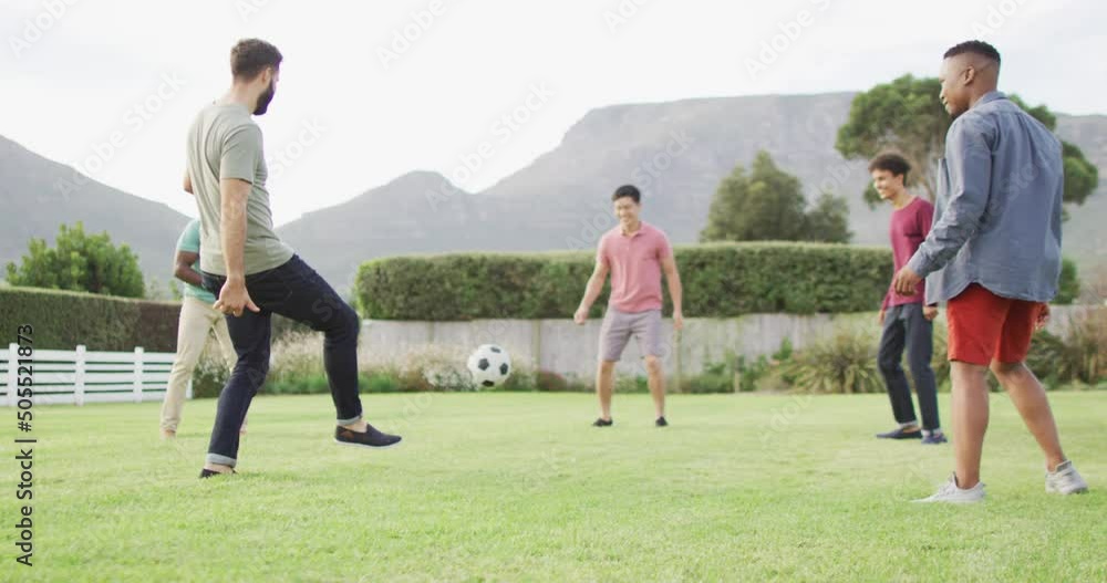 Happy diverse male friends playing football in garden on sunny day Happy diverse male friends playing football in garden on sunny day
