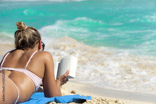 Blurred figure of a girl with a book in her hands against the background of blurry waves. A girl in a bikini is reading on the beach.