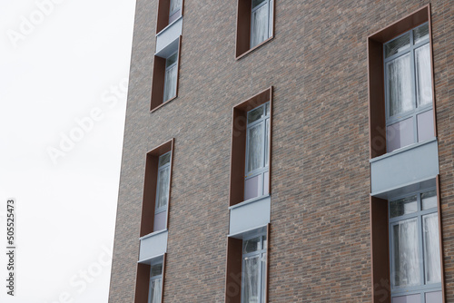 Modern brick and glass ventilated facade of the office building. A contrasting combination of sky and brick texture on a building. Architectural facade of a brown brick building..
