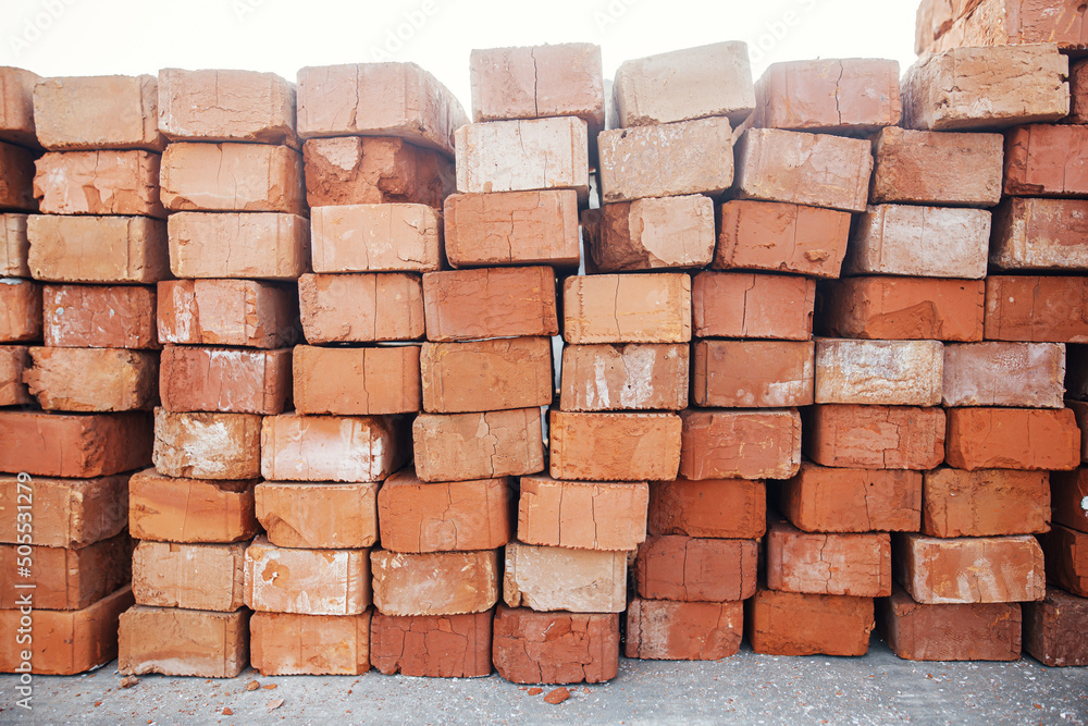 Obraz premium Stack of bricks masonry close up. Process of house building and building materials concept. Red bricks for laying at construction site. Brick wallpaper pattern