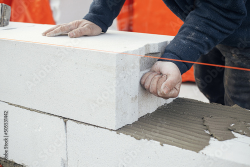 Masonry. Worker laying autoclaved aerated concrete blocks. Builder installing white blocks close up. Process of house building at construction site photo