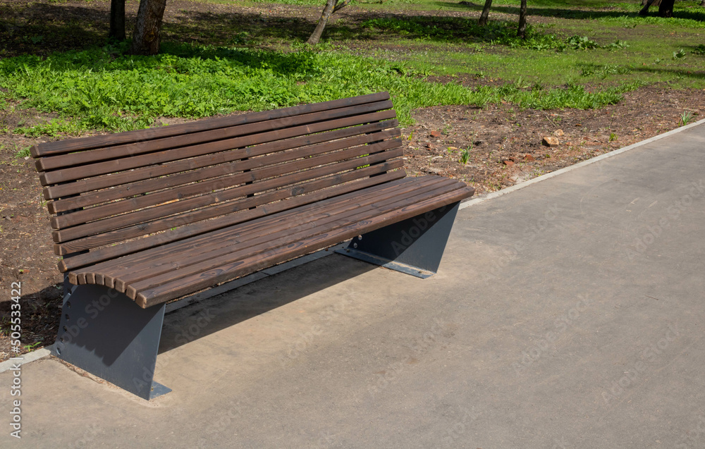 Wooden brown bench in the city park on a bright spring day