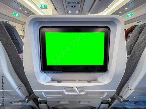 Airplane interior with green screen monitor on chair seat in front. In flight entertainment system with chroma key replaceable screen content for travel, tourism and vacation marketing