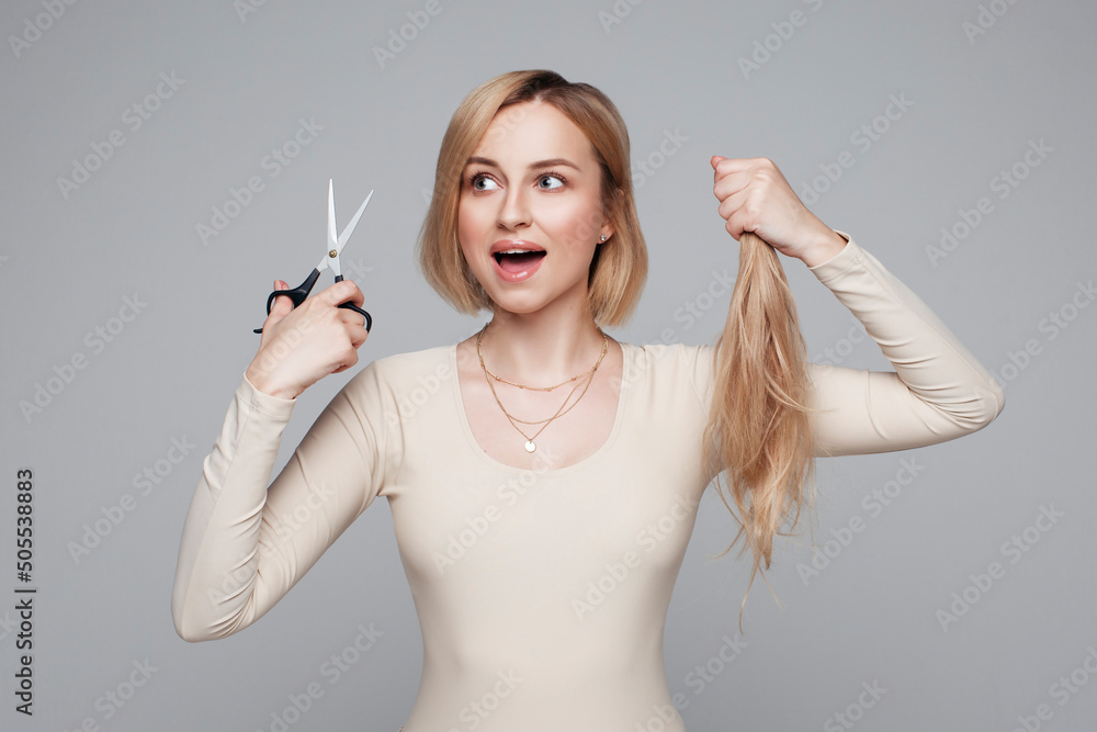 Φωτογραφία Studio portrait of blonde female cutting her own hair, hairstyle and haircut, lo