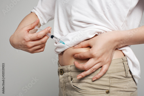 Studio close up of blonde caucasian woman holding needle making self injection in abdomen, health care, medicine treatment, vaccination, hormonal therapy, in vitro fertilization, isolated background