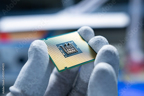 A CPU with clean, golden contacts held in the hand with some ESD gloves