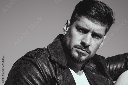 Portrait of a handsome young man with stylish haircut and beard in a leather jacket posing on the rocks. © alesgon