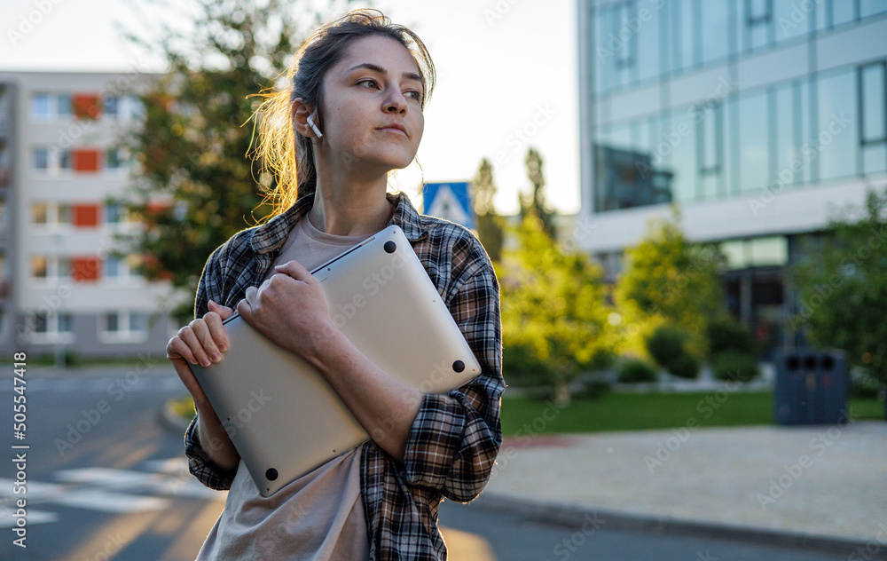 Fototapeta premium Front view. A girl in a shirt with a laptop on the street working. Remote work. c Сonducting online video calls. Freelance girl.