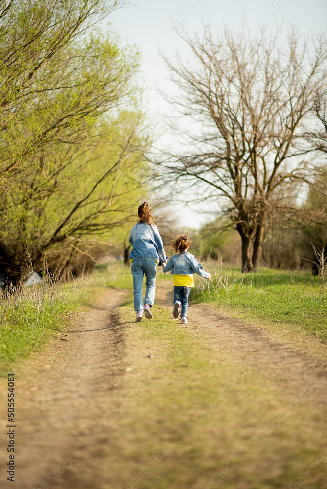 Fototapeta premium Two cute sister girls are running down an empty country road. Spring. Freedom. Childhood. Family.