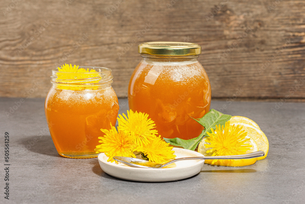 Dandelion jam or honey in the glass jar with fresh dandelion flowers. Trendy hard light, dark shadow Dandelion jam or honey in the glass jar with fresh dandelion flowers. Trendy hard light, dark shadow