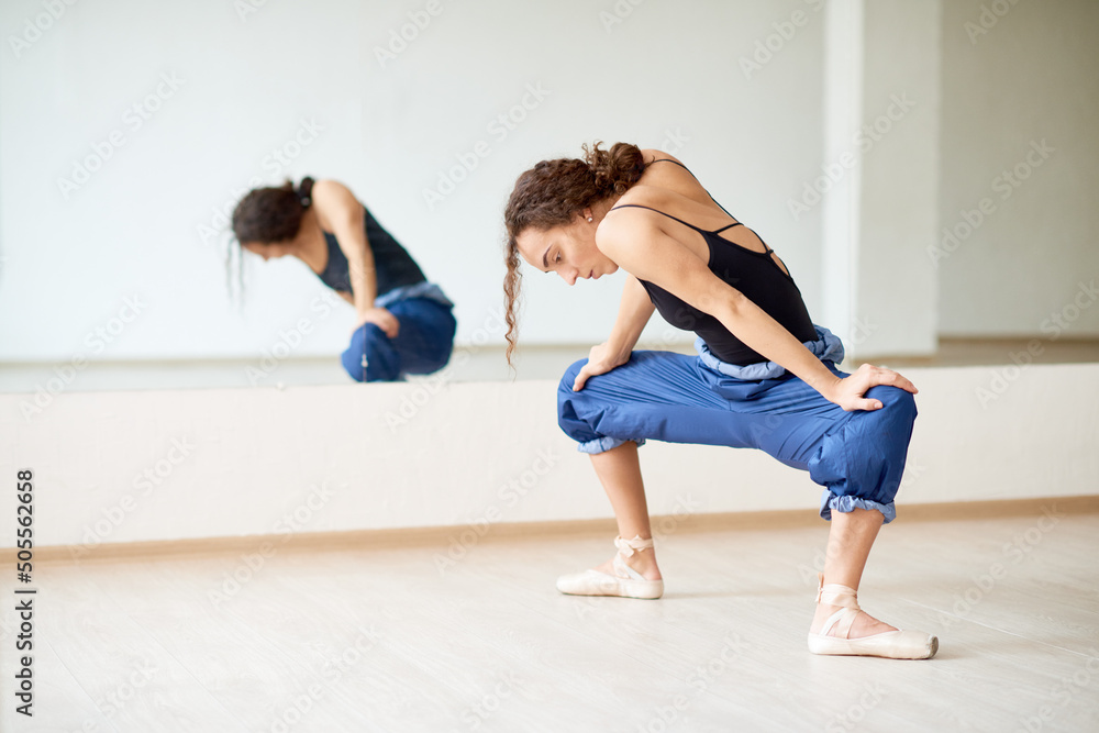 Young female ballet dancer stretching her body before rehearsal in dancing hall