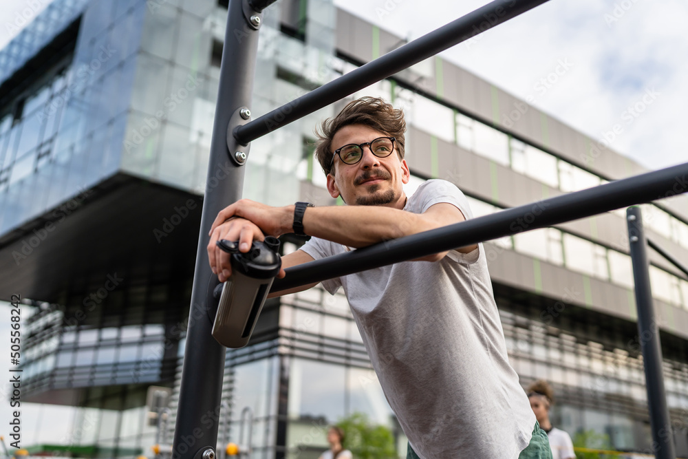 One caucasian man taking a brake during outdoor training in the park outdoor gym resting on the bars with supplement shaker in hand with water or supplementation happy smile real people copy space One caucasian man taking a brake during outdoor training in the park outdoor gym resting on the bars with supplement shaker in hand with water or supplementation happy smile real people copy space