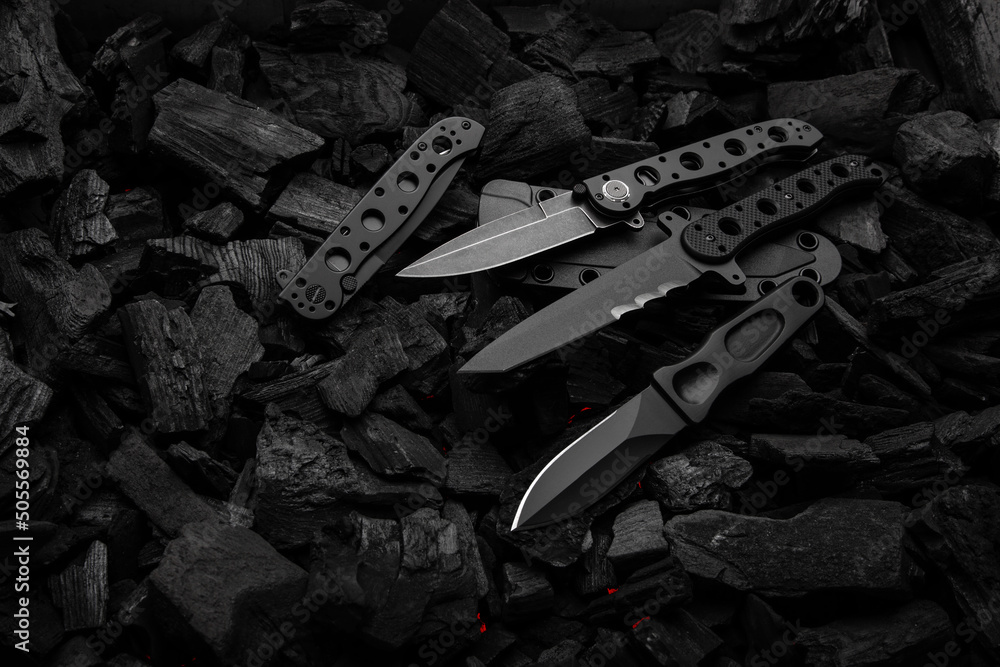Modern knives with black blades. Hunting, military and folding knives on smoldering charcoal. Black back. - obrazy, fototapety, plakaty 