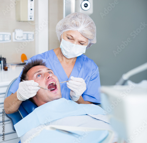 Professional dentist examining and performing treatment to young man