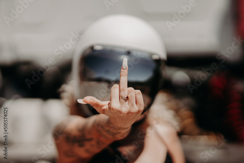 Cool rebellious motorcyclist girl in a helmet with tattoos showing middle finger