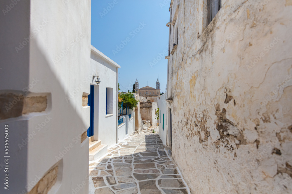 Paros, Greece - August 3, 2021: For the islands of the Cyclades archipelago typical narrow streets with white houses and blue roofs. Marble paved sidewalks. Located in the mediterranean Aegean Sea