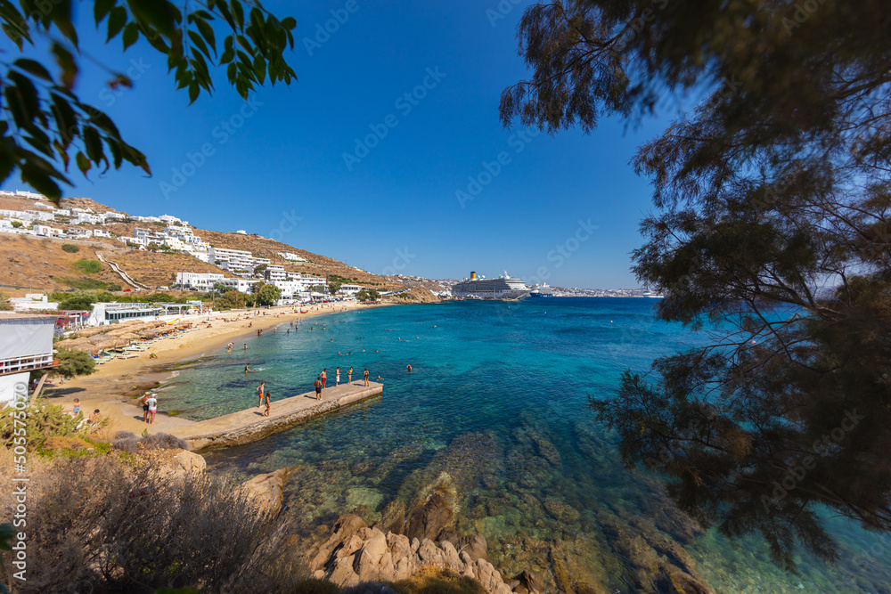 Mykonos, Greece - August 1, 2021: Panoramic wide angle view over the beach side of the island Mykonos. Mykonos is located in the cyclades archipelago in the Aegean Sea. Turquois water on sand beach.