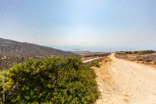 On an unsealed road at the island of Paros. Located at the cyclades archipelago. Horizon view over the vast dry landscape. Dusty sandy road under blue sky and hot sunshine. from the hills to the sea