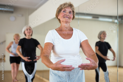 Portrait of a mature woman and people standing in the 1st position of the ballet stand at the mirror in a dance studio at a ..group lesson