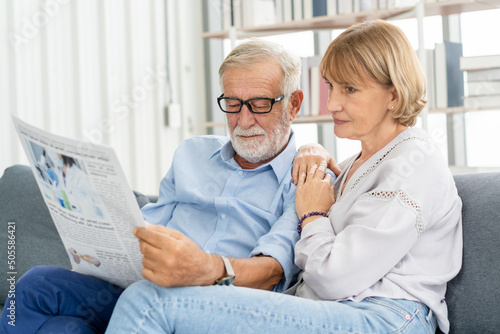 Happy husband and wife senior couple elderly family, caucasians mature, adult lover and retired man, woman reading newspaper, report on sofa together at home. Husband and wife lifestyle.