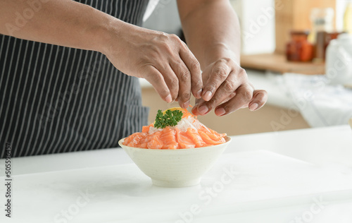 Senior man hand is decorating and prepare sliced salmon sashimi laid out on ice in a white Japanese style bowl served with sliced lemon and radish at kitchen. Japanese food home cooked concept