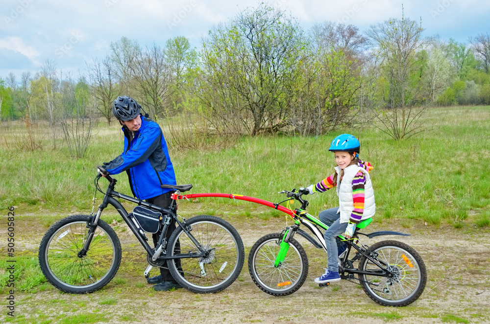 Family cycling, father teaches child to ride bicycle with bike tow bar, family sport and activity with kid outdoors