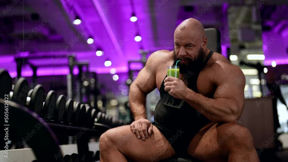 A mature male bodybuilder drinks an energy drink made of fruit during a