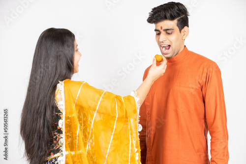 Young Indian brother and sister celebrating Diwali, rakshabandhan or bhai dooj festival isolated on white studio background. enjoying sweet laddo,