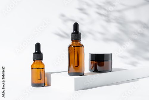 Fotografia Natural cosmetics in amber glass packaging on white background with flowers shadows