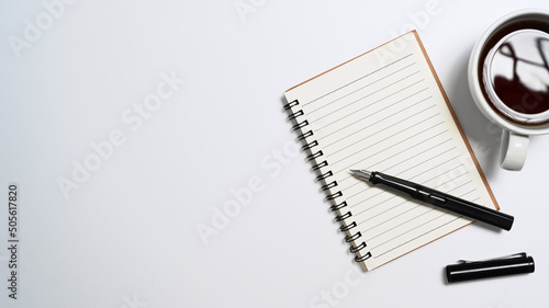 Notebook, coffee cup and pen on white background. Top view with copy space