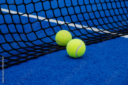 Two balls near the net of a blue artificial grass paddle tennis court. © Vic