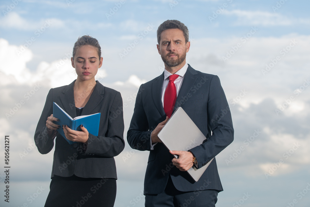 Successful business couple. Businessman and businesswomen. Successful business people standing over blue sky. Man hold laptop woman with notebook. Successful business couple. Businessman and businesswomen. Successful business people standing over blue sky. Man hold laptop woman with notebook.