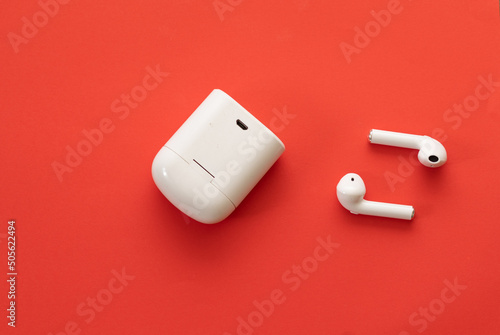 top view of Small white wireless headphones near their holster - on a red background