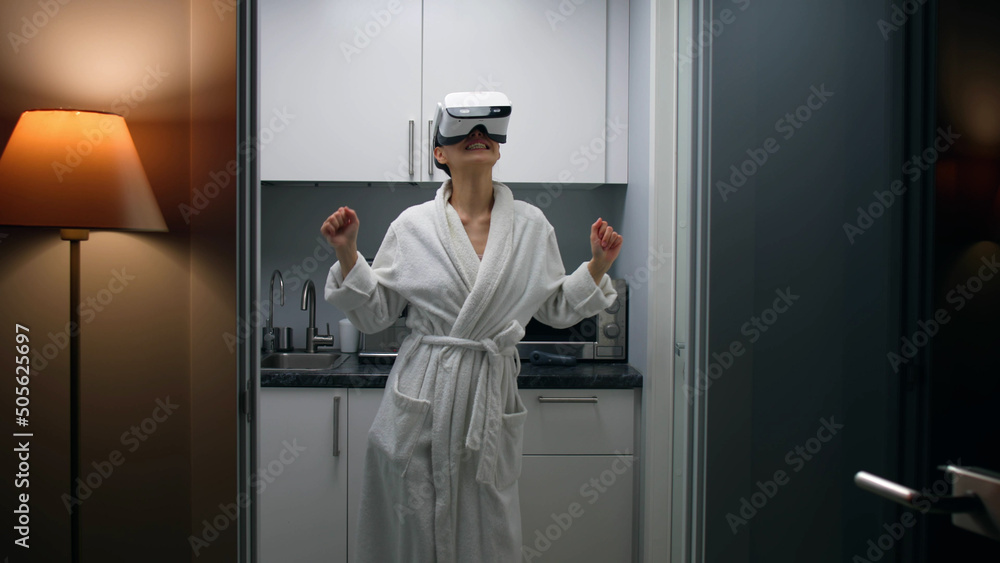Young woman in bathrobe and augmented reality headset dancing in small kitchen Young woman in bathrobe and augmented reality headset dancing in small kitchen