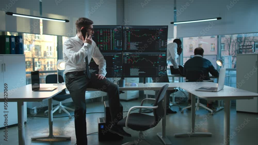 Businessman talk on smartphone sitting at desk with multiple screens with financial data Businessman talk on smartphone sitting at desk with multiple screens with financial data