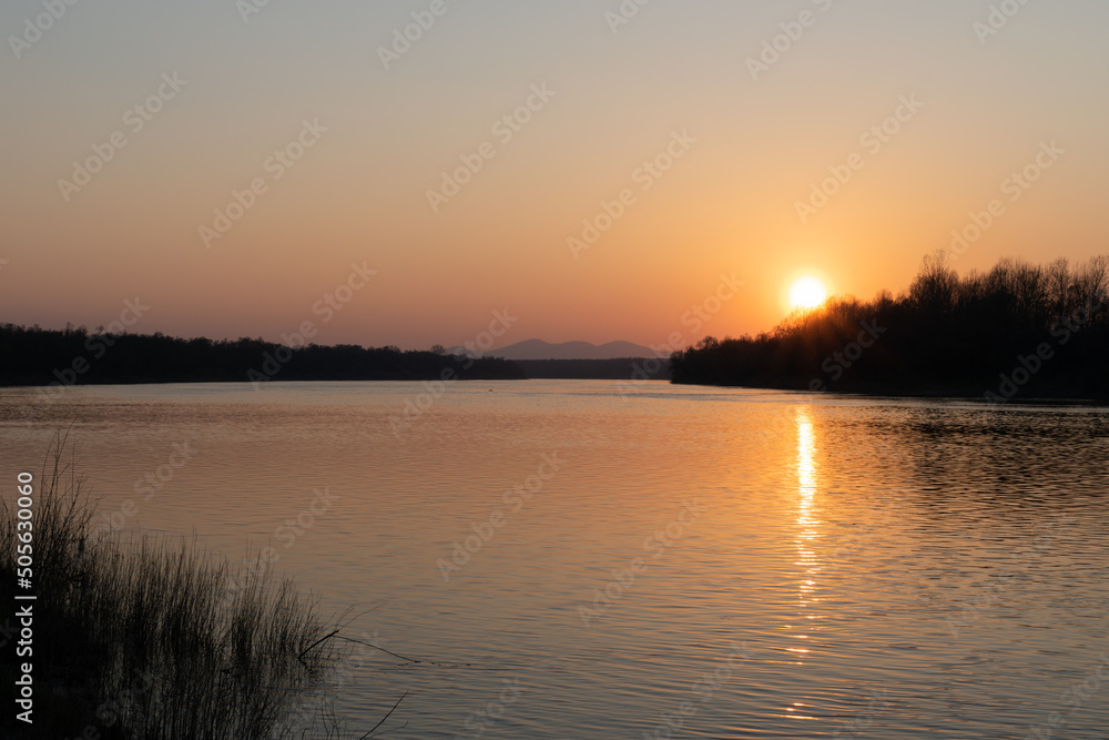 Landscape of river and mountantain before sunset, rippling water and distant mountain in haze with sun on clear sky, calming fair weather in nature
