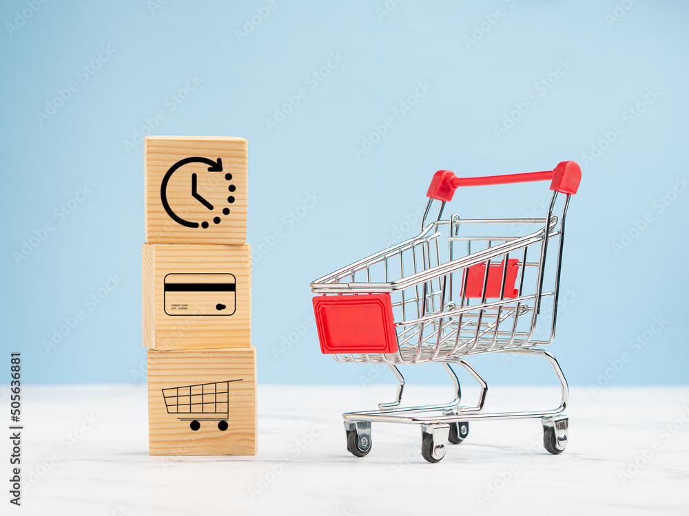 Wooden cubes with icons of the time, a credit card, and a shopping trolley. A mini shopping trolley over a marble floor against a blue background