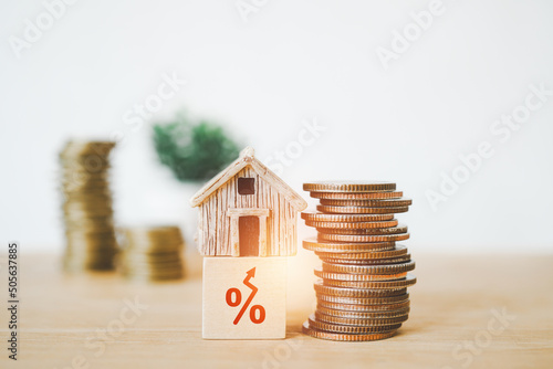 miniature house on wooden cube block with red increasing percent and stack of coins