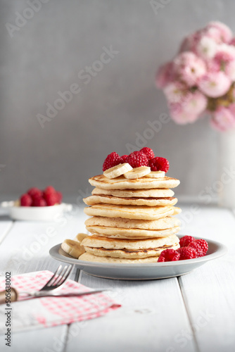 American pancakes with raspberries and bananas over bright minimal background. Delicious pancakes on wooden table with fruits. 