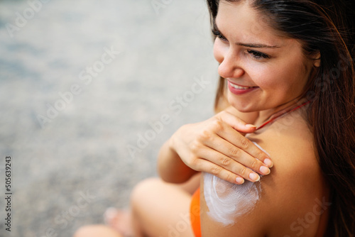 Attractive woman with healthy skin applying sunscreen to shoulder on summer vacation at beach