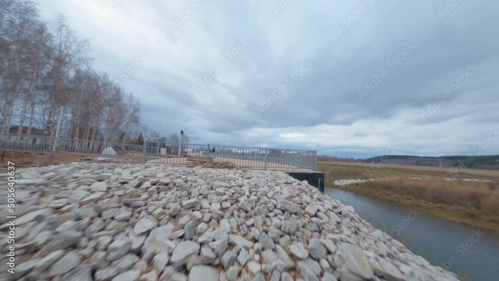 Motion under bridge to building embankment road with construction materials in new city park on spring day drone first point view Motion under bridge to building embankment road with construction materials in new city park on spring day drone first point view