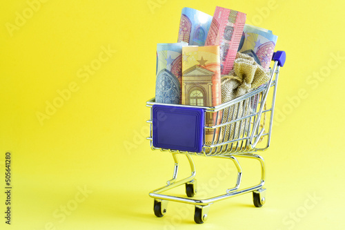 Concept economic. Shopping cart with euro banknotes, yellow background and copy space.
