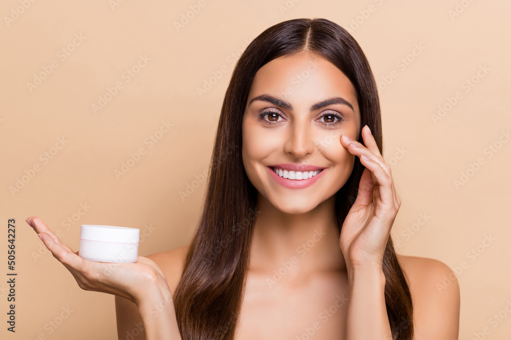Portrait of attractive cheery girl holding on palm daily cream applying on soft skin isolated over beige pastel color background Portrait of attractive cheery girl holding on palm daily cream applying on soft skin isolated over beige pastel color background