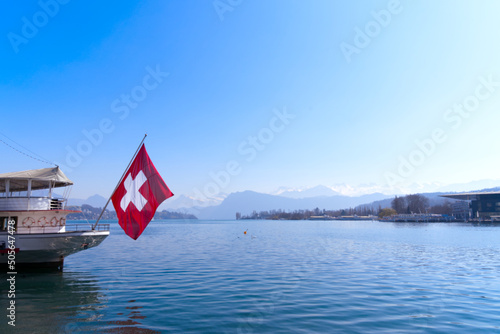Stern of passenger ship at Lake Lucerne with waving Swiss flag ans Swiss Alps in the background on a sunny spring day. Photo taken March 23rd, 2022, Lucerne, Switzerland.