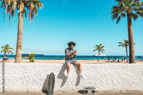 African man having fun doing selfie with mobile phone with beach on background - Focus on face photo