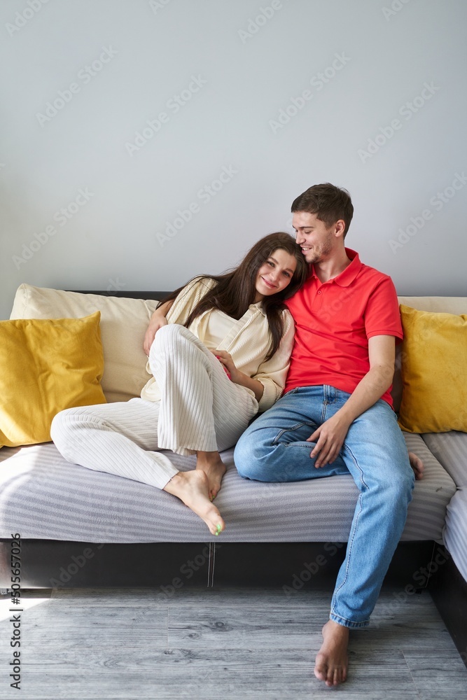 a young couple are sitting side by side on the sofa, the woman rested her head on the shoulder of the man. the concept of a happy young family, tenderness, home comfort, love and harmony in a couple a young couple are sitting side by side on the sofa, the woman rested her head on the shoulder of the man. the concept of a happy young family, tenderness, home comfort, love and harmony in a couple