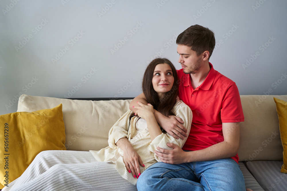 young couple hugging at home, sitting on the couch and tenderly look at each other. the concept of a happy young family, tenderness, home comfort, love and harmony in a couple young couple hugging at home, sitting on the couch and tenderly look at each other. the concept of a happy young family, tenderness, home comfort, love and harmony in a couple