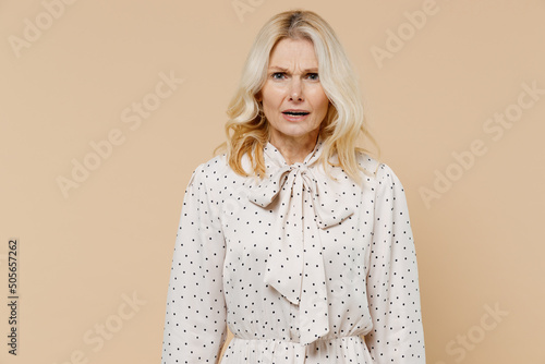 Irritated dissatisfied elderly gray-haired blonde woman lady 40s years old wears pink dress looking camera isolated on plain pastel beige background studio portrait. People emotions lifestyle concept. photo