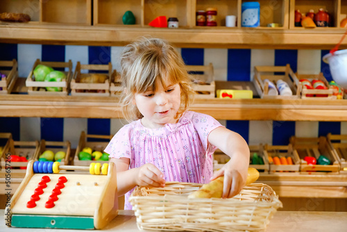 Little preschool girl play with food and grocery wooden toys. Happy active child playing role game as cashier or seller, in wood shop or supermarket. Education, activity for kids. photo